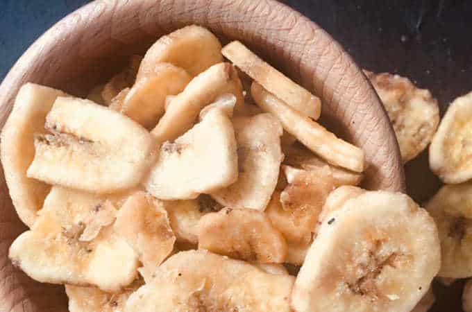 Chipsy bananowe słodzone w drewnianej misce i rozsypane obok niej