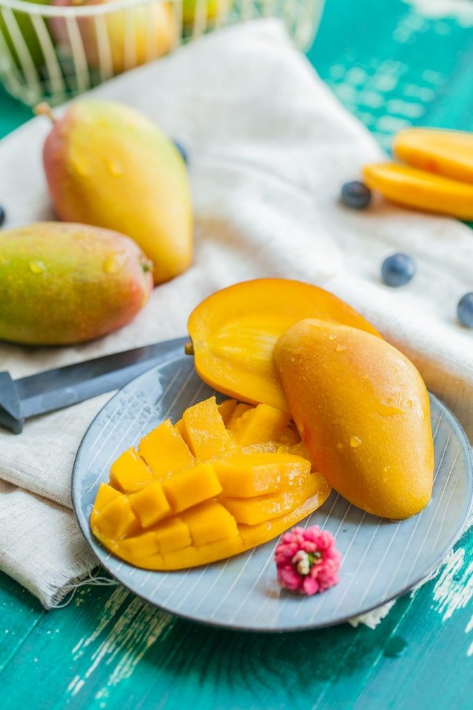 świeże mango przekrojone na talerzu z owocami w tle i nożem obok