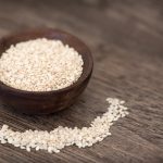 sezam biały w drewnianej misce i rozsypany na stole