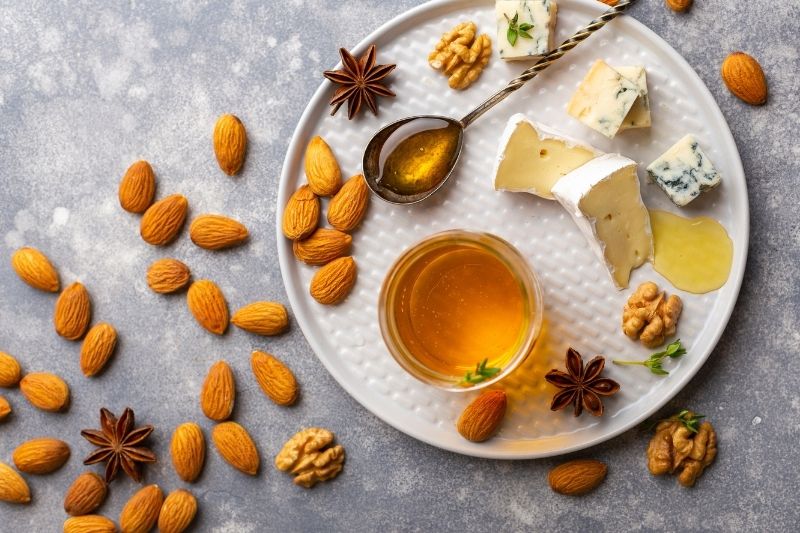 Zbliżenie na talerz wypełniony rozmaitymi produktami: migdały, orzechy włoskie, serki i miód