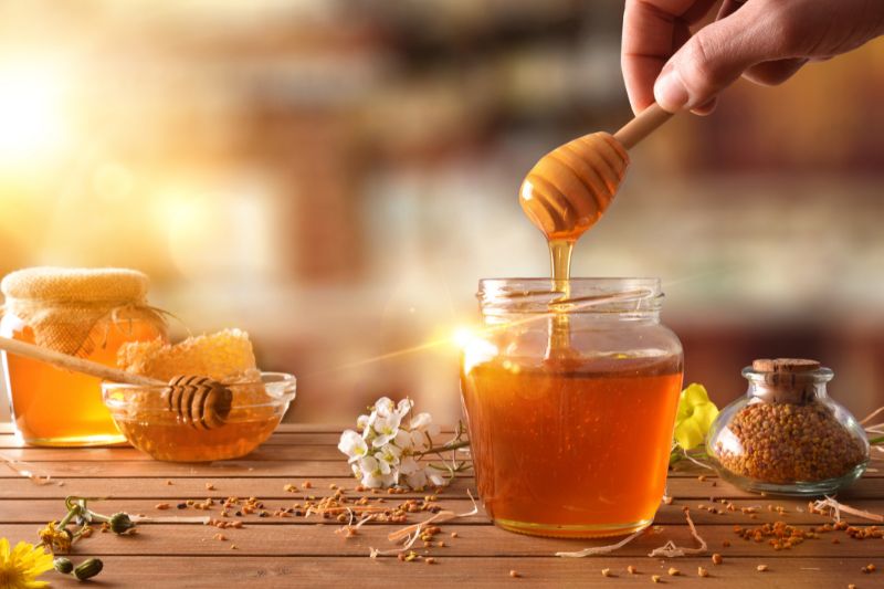 Zbliżenie na słoik miodu naturalnego na drewnianym stole, obok podobne produktu