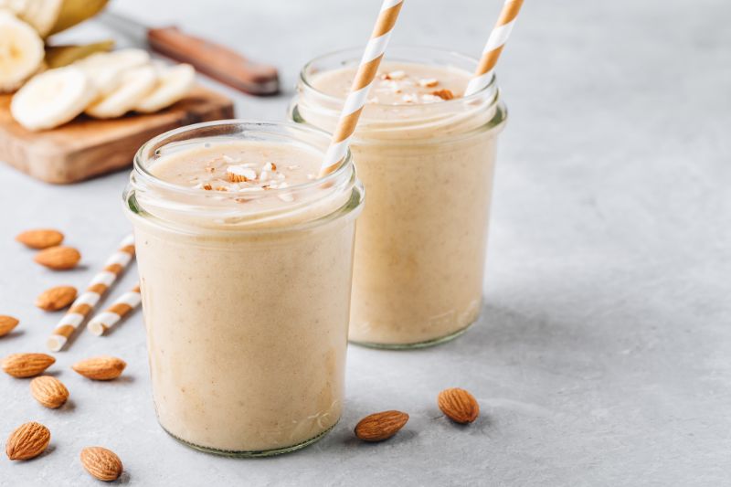 Dwa szklane słoiczki z smoothie cynamonowym, na blacie rozsypane migdały