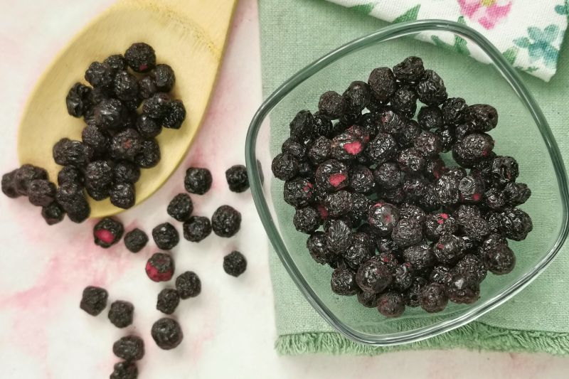 Aronia liofilizowana w szklanej misce i na drewnianej łyżce obok