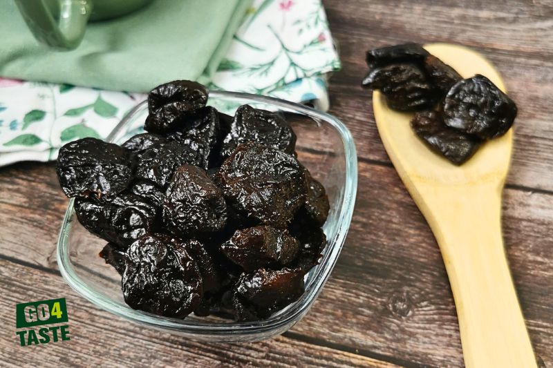Szklana miska z suszonymi śliwkami, obok drewniana łyżka z produktem
