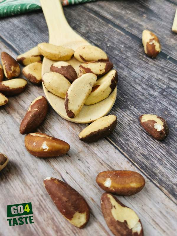 Zbliżenie na orzechy brazylijskie na drewniane łyżeczce oraz rozsypane na stole