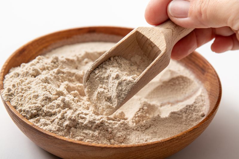 Zbliżenie na proszek z łuski psyllium w misce i na drewnianej szpatułce