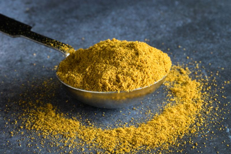 metalowa łyżka z curry, trochę przyprawy zostało rozsypane na blat