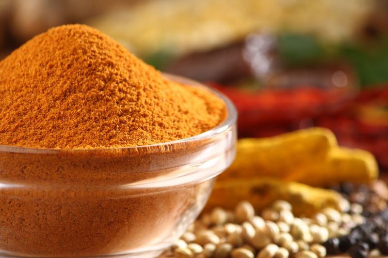 Szklana miska wypełniona przyprawą curry, na tle różne produkty spożywcze