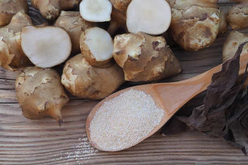 Na drewnianej łyżce znajduje się inulina, obok leża bulwy topinamburu