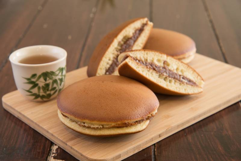 Zbliżenie na potrawe Dorayaki leżącą na drewnianej desce obok kubka