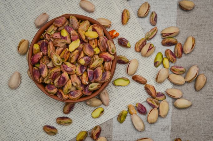 Prażone pistacje w miseczce oraz rozsypane pistacje w łupinach